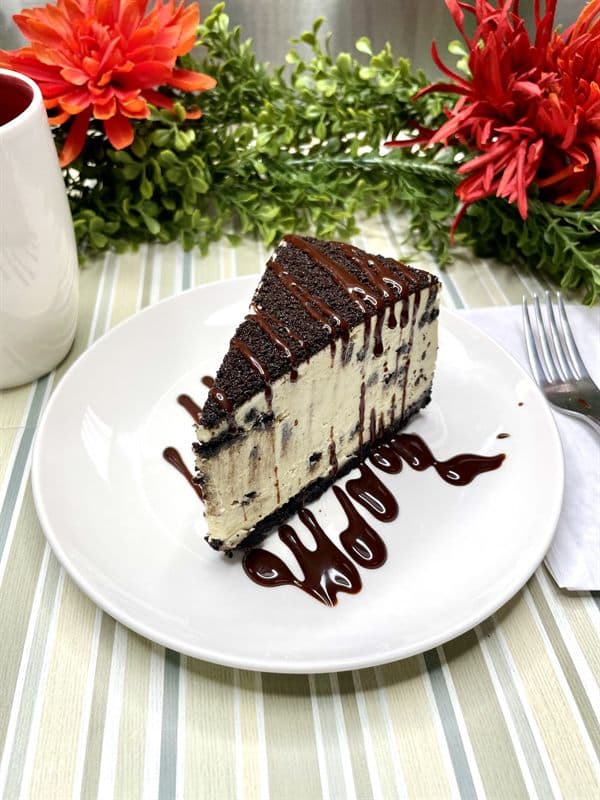 A slice of Oreo cheesecake with cookie-crumb topping and dark chocolate drizzle.