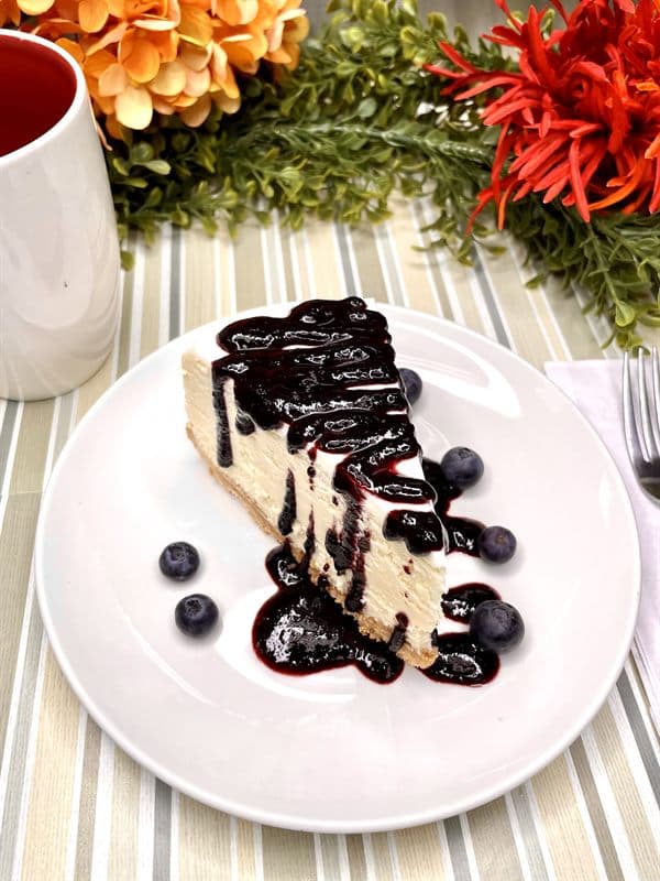 A slice of cheesecake with blueberry sauce and fresh blueberries.