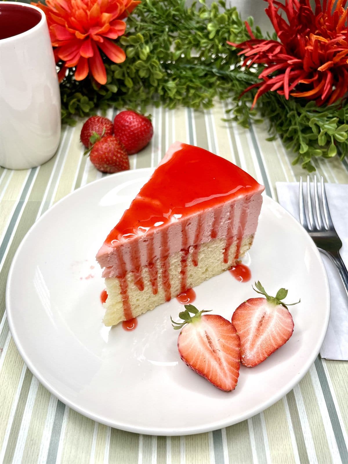 A slice of strawberry cheesecake with a glossy red glaze, served with fresh strawberries.