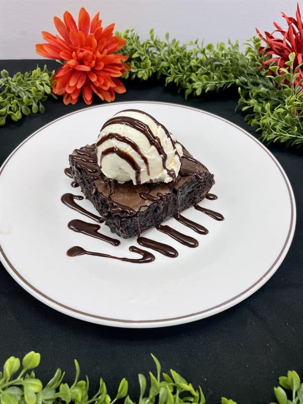 A warm brownie topped with a scoop of vanilla ice cream and chocolate sauce.