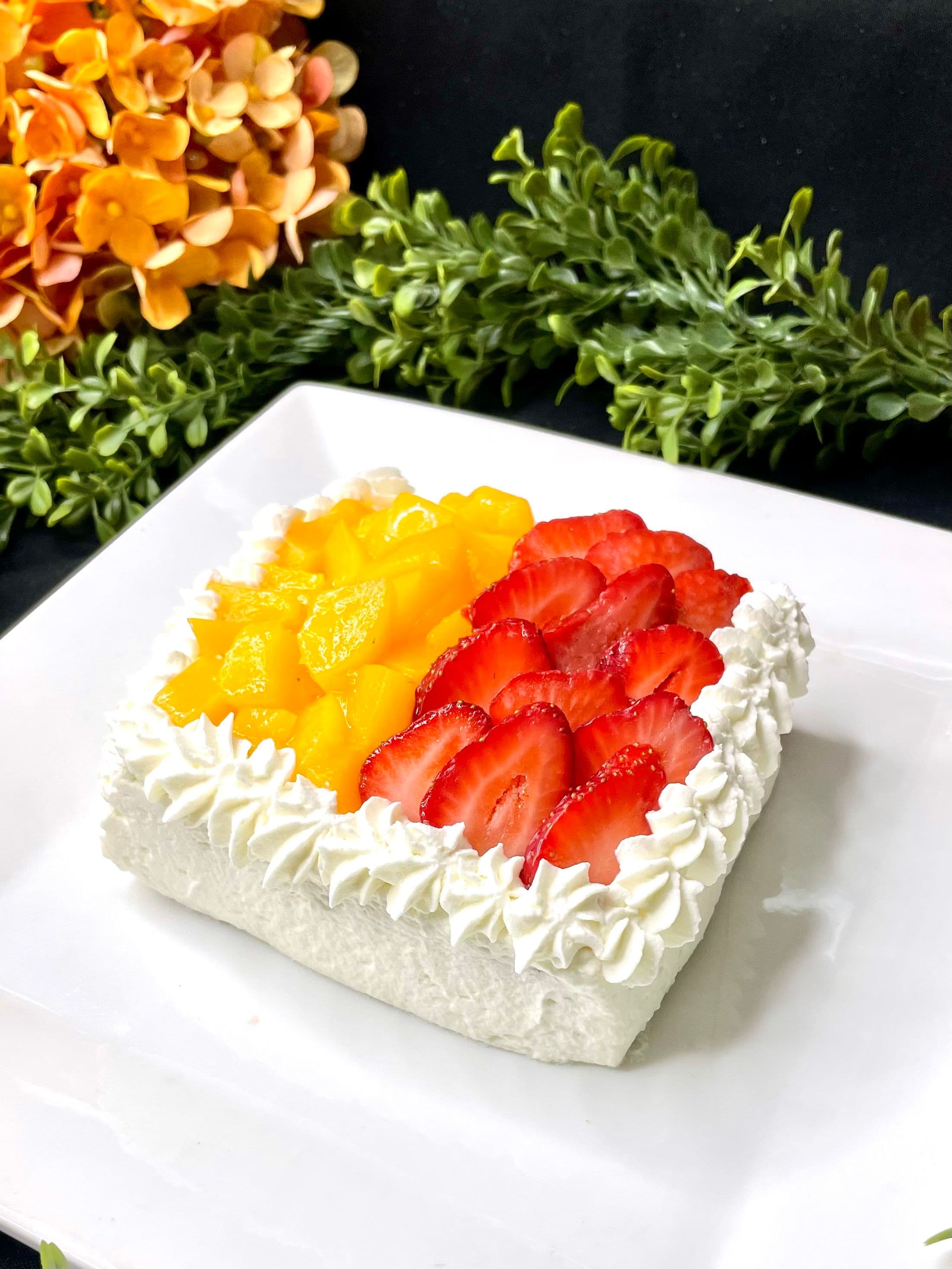 A square slice of tres leches cake piped with whipped cream and crowned with fresh strawberries and mango.