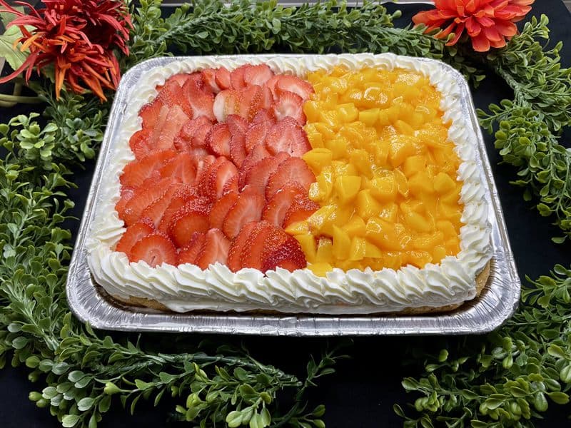 A tres leches party tray topped with fresh strawberries and mango.
